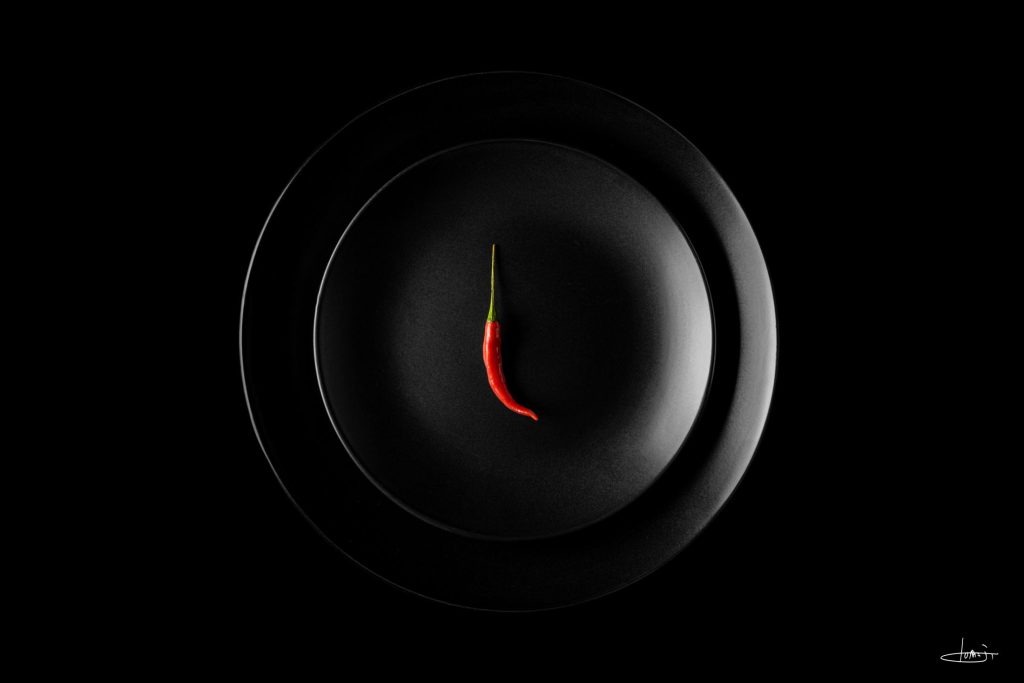 Red Malagueta over two black plates, in a minimalist photographic composition.